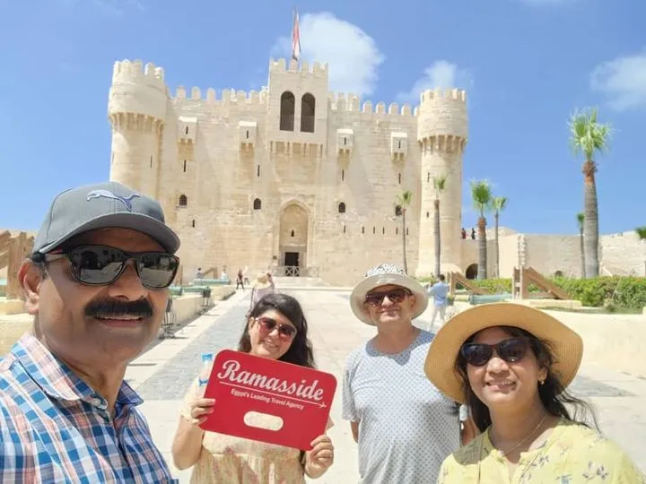 Tourists holding a Ramasside Tours sign in front of the Citadel of Qaitbay during an Alexandria Day Tour.