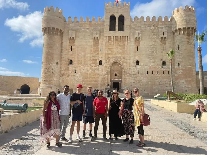 Alexandria Day Tours guide in red uniform with a diverse group of travelers at the Citadel of Qaitbay.