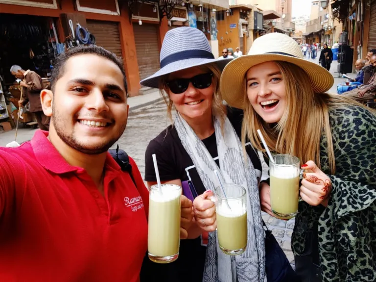 A friendly Ramasside tour guide sharing sugarcane juice with two female tourists in a Cairo market street.