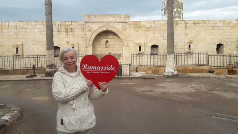 A smiling female traveler holding a heart-shaped Ramasside Travel Agency sign in a historic Egyptian street at night.