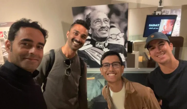 Four tourists smiling in front of Anwar Sadat’s portrait at the Bibliotheca Alexandrina museum during a guided tour.